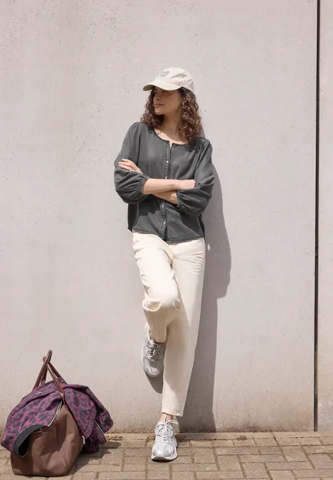 3/4-Arm Jeansbluse mit Rundhals tencel grey Frau lehnt mit verschränkten Armen an heller Wand, trägt Cap, weiße Hose und Sneaker, Tasche liegt am Boden.