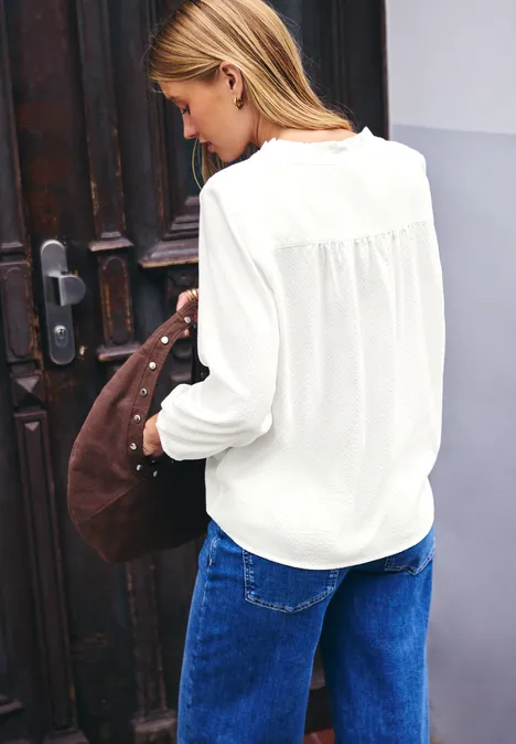 Frau von hinten in weißer Bluse und blauen Jeans, schultert Tasche, steht vor einer Holztür.