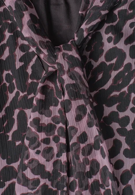 Close-up van een blouse met paars-zwarte luipaardprint en een decoratieve strik bij de kraag.