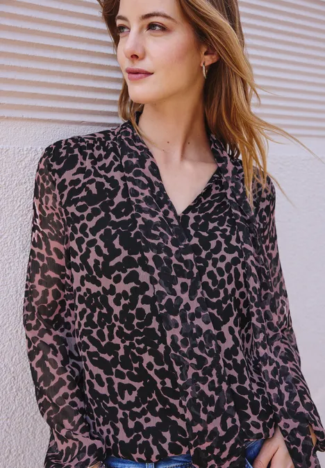 Jonge vrouw in luipaardprint blouse voor een lichte muur, kijkt opzij.
