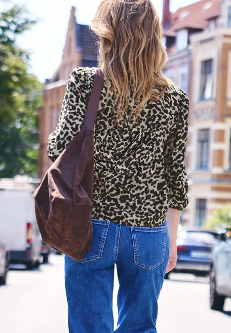 Vrouw van achteren in jeans en luipaardtop met schoudertas op een woonstraat.