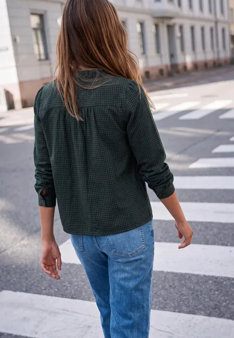 Eine Frau mit Jeans und dunkelgrüner Bluse überquert einen Zebrastreifen in der Stadt.