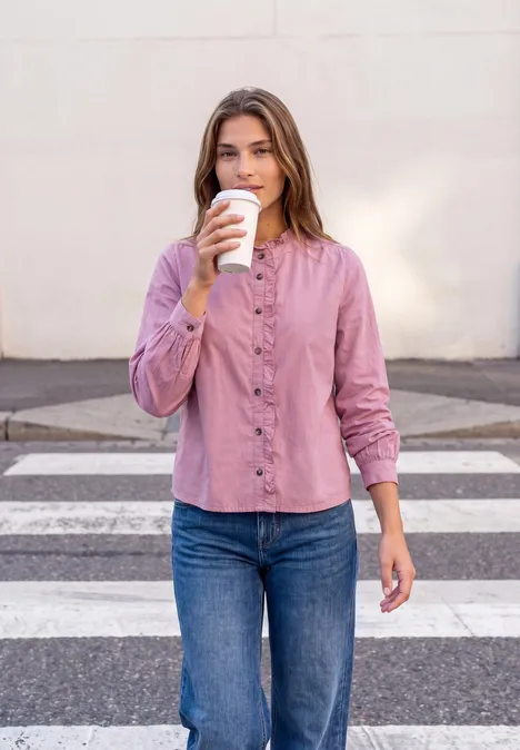 Frau in rosa Bluse und Jeans trinkt Coffee-to-go beim Überqueren eines Zebrastreifens.