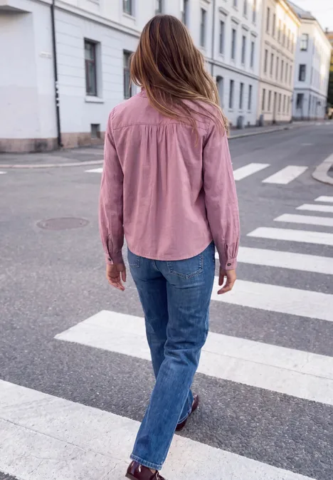Frau im rosa Oberteil und blauer Jeans läuft über einen Zebrastreifen in einer Stadtstraße