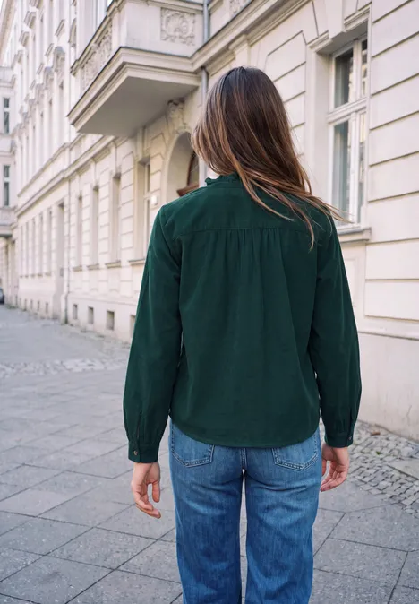 Person in grüner Bluse und blauen Jeans von hinten vor eleganter, historischer Häuserfassade.