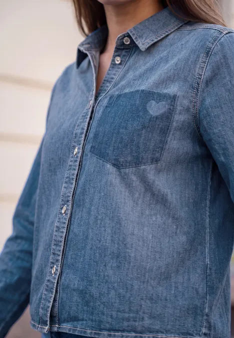 Eine Person trägt eine blaue Jeansbluse mit Knopfleiste und Brusttasche.