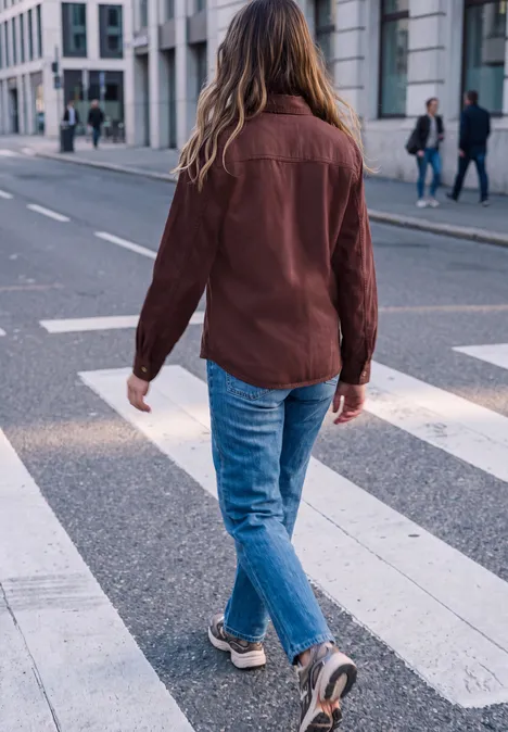 Eine Person mit braunem Hemd und blonden Haaren geht über einen Zebrastreifen in der Stadt.