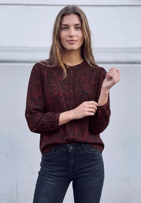 3/4-Arm Tunika mit Rundhals und Snake-Print russet red Eine junge Frau in dunkler, schlangenmusternder Bluse und schwarzen Jeans steht vor weißer Wand, lächelt.