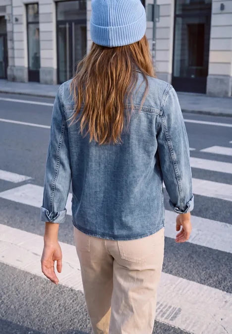 Een persoon in een denimshirt en muts steekt de straat over op een zebrapad.
