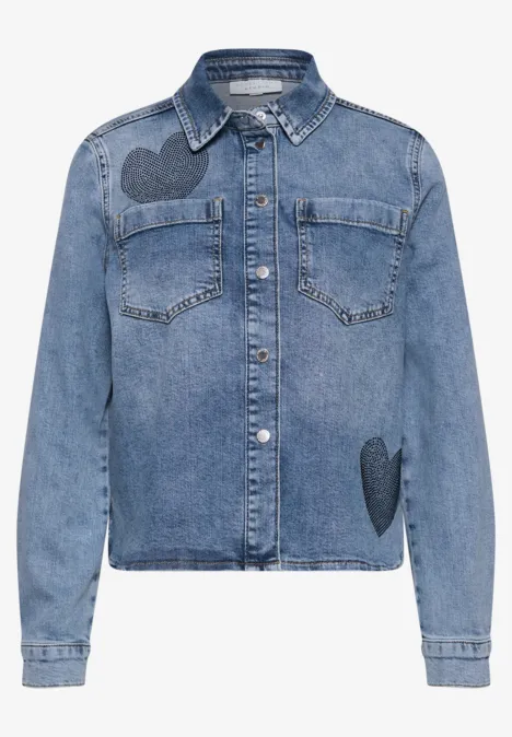 Blauw spijkerjasje met overhemdkraag, knopen, borstzakken en hartpatches op schouder en heup.