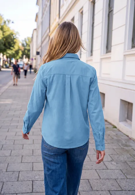 Chemisier en velours côtelé avec motif en forme de cœur loom blue Frau von hinten in Jeanshemd und Jeans spaziert auf städtischem Gehweg.