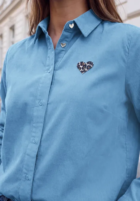 Chemisier en velours côtelé avec motif en forme de cœur loom blue Frau trägt hellblaues Hemd mit leopardgemustertem Herz-Patch auf der Brust.