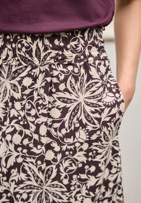 Midi-Rock mit Volants und Print very berry Nahaufnahme: Person trägt bequeme Hose mit elastischem Bund und weißem Blumenmuster auf lila Stoff.