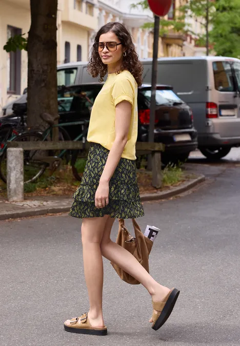 Knielanger Chiffon-Rock mit Print maritime blue Eine Frau in gelbem T-Shirt, gemusterter Rock und Sandalen läuft mit Tasche eine Straße entlang.