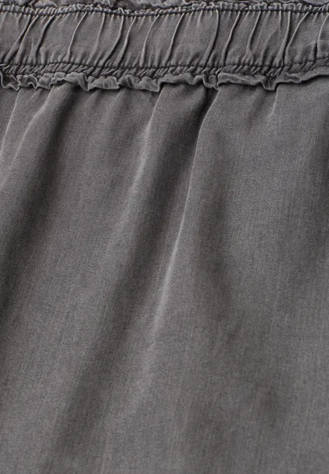 Close-up van grijze stof met elastische tailleband en subtiele plooien.