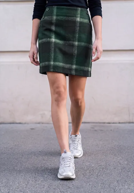 Vrouw in groene ruitrok en witte sneakers loopt over straat