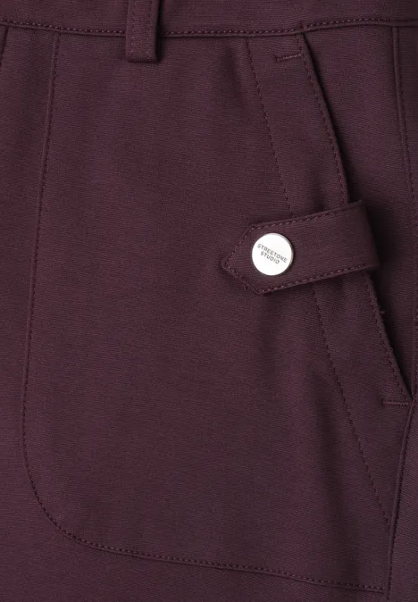 Seitentasche eines dunkelvioletten Kleidungsstücks mit Zierlasche und Metallknopf.