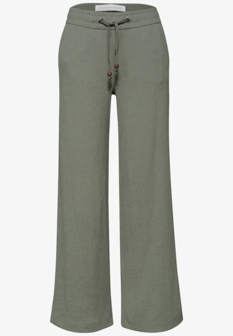 Pantalon fluide en lin vert olive, taille ajustable par cordon, coupe ample et confortable.