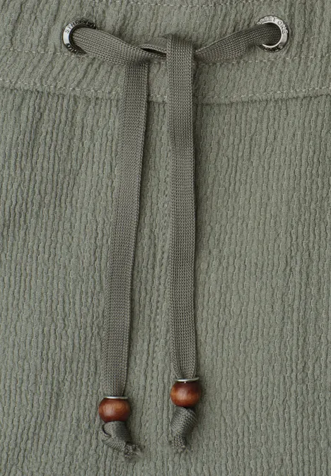 Nahaufnahme eines strukturierten Stoffbundes mit Tunnelzug und Holzperlen