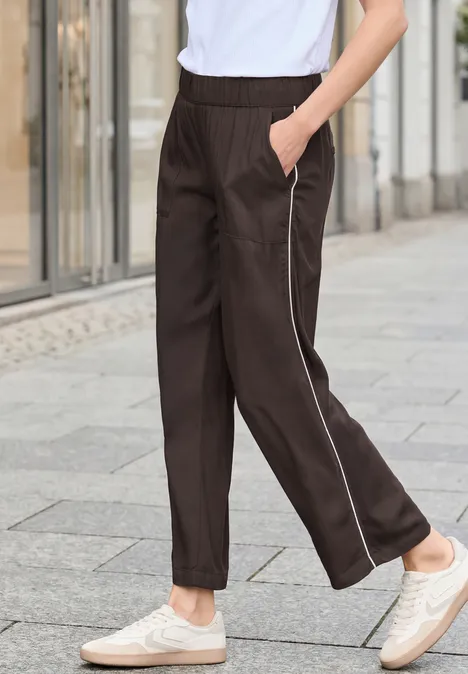 Person geht auf Steinpflaster, trägt schwarze Hose mit seitlichem weißen Streifen und cremefarbene Sneaker.