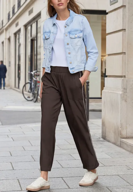 Person läuft in weißem T-Shirt, heller Jeansjacke und dunkler, lässiger Hose auf der Straße.
