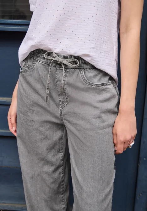 Graue Jeanshose mit Kordelzug an der Taille, kombiniert mit einer hellen Bluse.