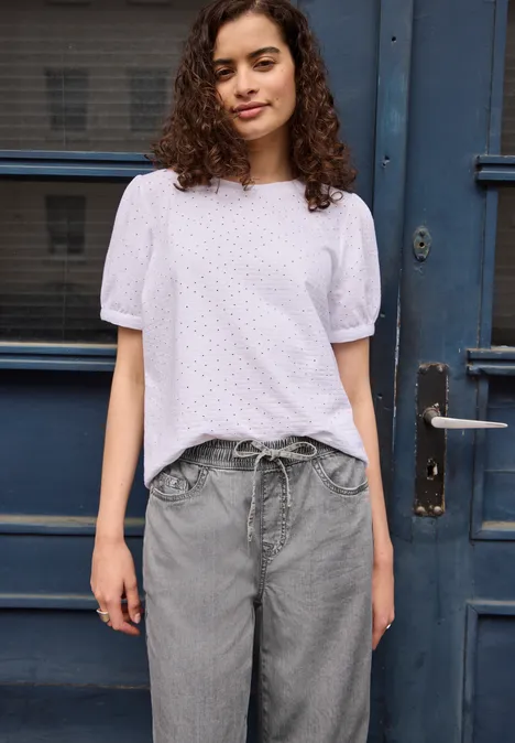 Person mit weißer Bluse und grauer Hose steht vor blauem Türportal.