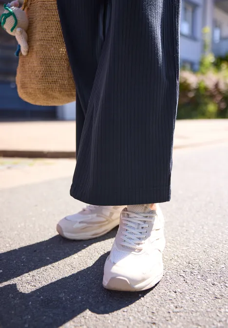 Wide Leg Hose in Rippstruktur midnight muse Weiße Sneaker, weite dunkelblaue Hose, Basttasche, sonnige Straßenszene.