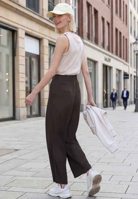 Person in weißem Top und weiter, dunkler Hose spaziert in einer ruhigen Einkaufsstraße.