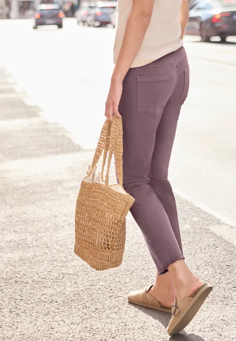 Iemand met paarse broek en sandalen loopt langs de straat en draagt een gevlochten strotas.