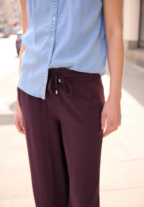 Persoon met mouwloos lichtblauw hemd en bordeauxrode broek, zichtbaar vanaf de taille.