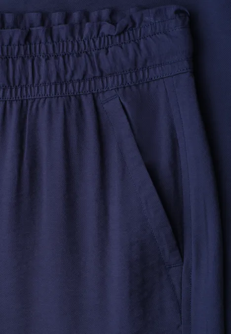 Close-up van een donkerblauwe broek met elastische tailleband en zijzak.