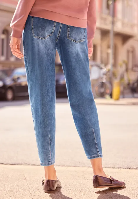 Rückenansicht einer Person in Jeans, Pullover und Loafern auf einem Bürgersteig.
