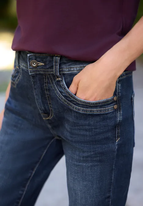 Mid Waist Bootcut Jeans im Slim Fit intense dark blue Hand steckt in der Tasche einer dunkelblauen Jeans, dazu ein violettes Oberteil
