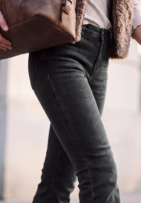 Bootcut-jeans met Mid Waist-taille in Slim Fit authentic black washed Person trägt enge schwarze Jeans, beige Jacke und hält braune Ledertasche.