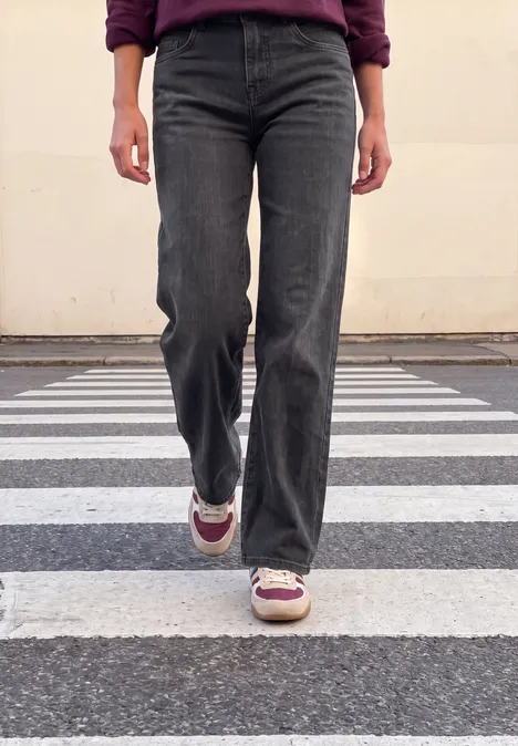 Mid Waist Wide Leg Jeans im Casual Fit soft black washed Eine Person in schwarzen Jeans und Sneakers läuft über einen Zebrastreifen, nur die Beine sichtbar.