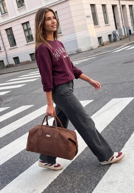 Mid Waist Wide Leg Jeans im Casual Fit soft black washed Frau in lässiger Kleidung überquert einen Zebrastreifen und trägt eine braune Reisetasche.
