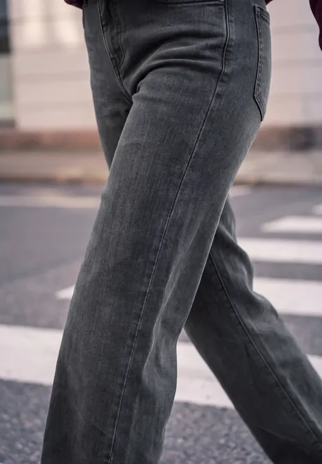 Mid Waist Wide Leg Jeans im Casual Fit soft black washed Eine Person trägt weite graue Jeans und geht über einen Fußgängerüberweg.