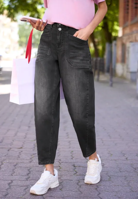 Person trägt schwarze baggy Jeans, pinkes Oberteil, weiße Sneaker und geht auf einem Gehweg.