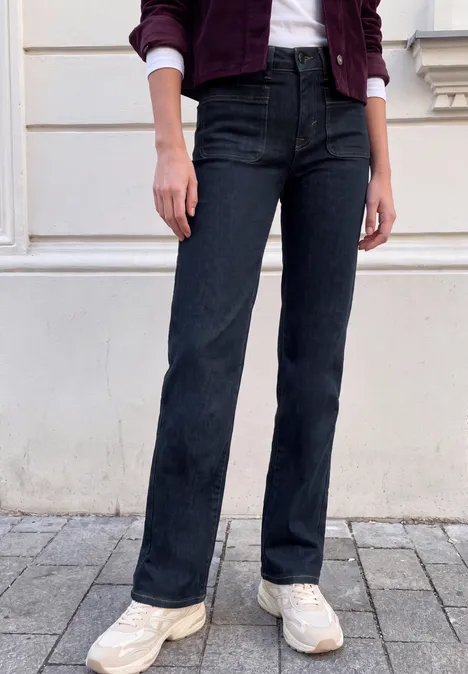Mid Waist Wide Leg Jeans im Loose Fit rinsed blue washed Eine Person trägt dunkelblaue, gerade geschnittene Jeans und weiße Sneaker vor einer weißen Hauswand.