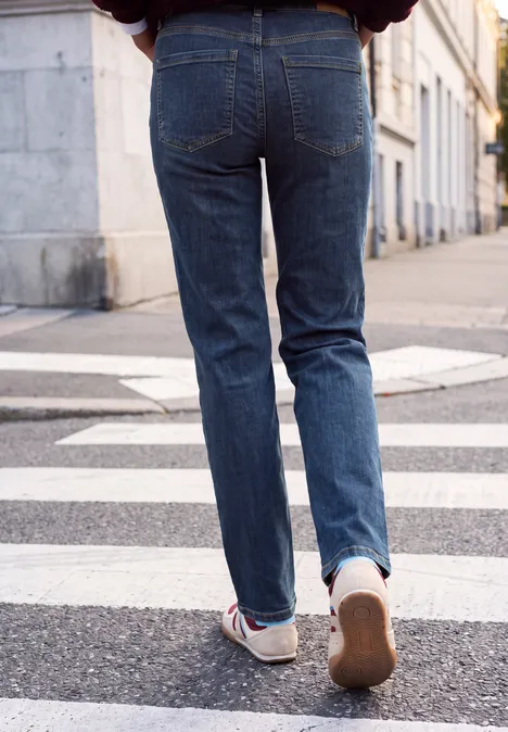 Mid Waist Straight Leg Jeans im Casual Fit dark blue random washed Hinteransicht einer Person in blauen Jeans und Turnschuhen, die über einen Zebrastreifen läuft.