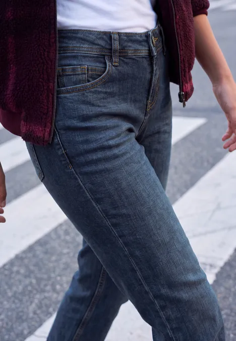 Mid Waist Straight Leg Jeans im Casual Fit dark blue random washed Nahaufnahme einer Person in blauen Jeans und burgunderrotem Oberteil auf einem Zebrastreifen.