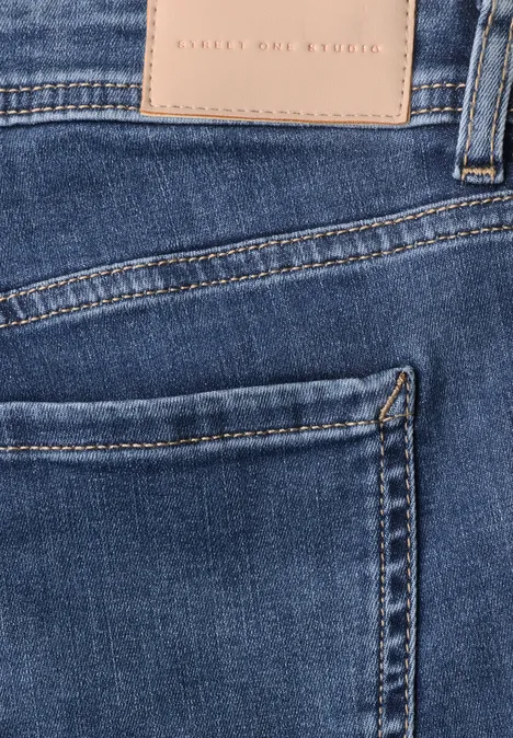 Mid Waist Slim Leg Jeans im Casual Fit medium blue washed Nahe Ansicht einer blauen Jeans-Tasche mit hellbraunem Label-Patch am Bund.