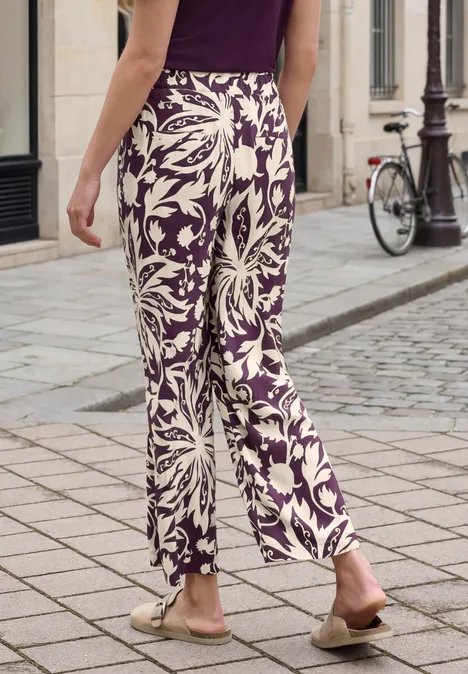 Wijde broek met paars-witte bloemenprint, gedragen op een stenen straat.