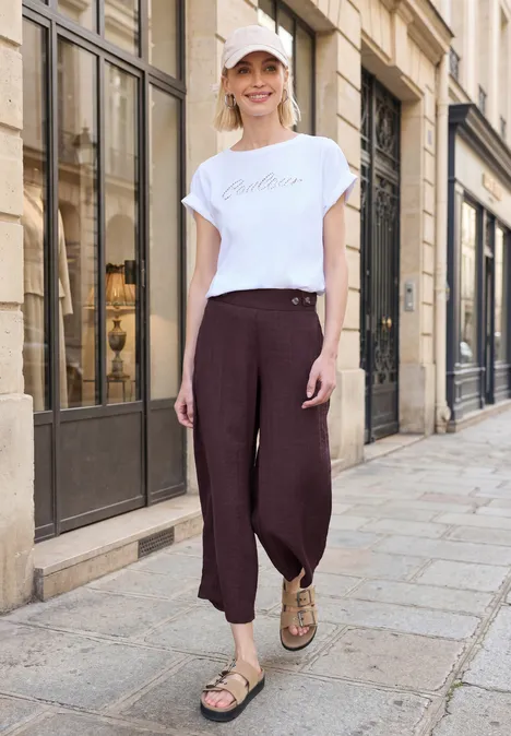 Person mit weißem T-Shirt und weiten, braunen Hosen läuft auf gepflasterter Straße an Hausfronten vorbei.