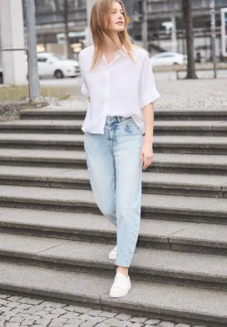 Frau in weißem Hemd und Jeans läuft lässig Treppe hinab in urbaner Umgebung.