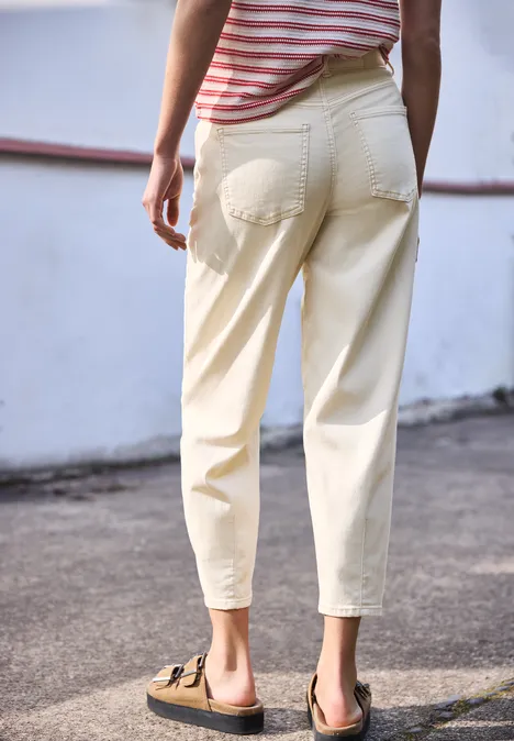 Iemand staat met de rug naar de camera, draagt een lichte broek en bruine sandalen op een geplaveide ondergrond.