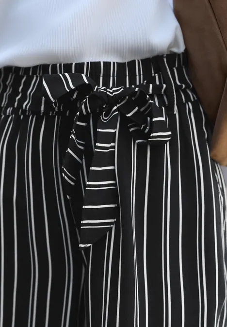 Zwarte wijde broek met witte verticale strepen en een strikceintuur in de taille.