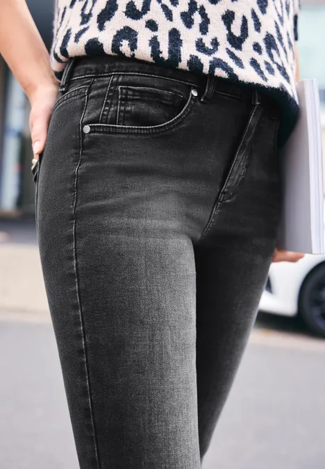 Mid Waist Skinny Leg Jeans im Skinny Fit black washed Eine Person trägt schwarze Jeans und hält eine Mappe oder ein Buch in der Hand.