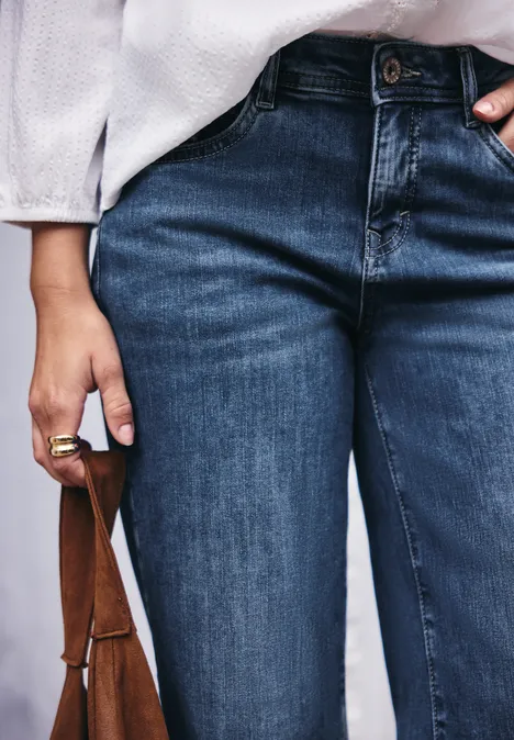 Mid Waist Wide Leg Jeans im Loose Fit bright mid blue washed Person trägt dunkelblaue Jeans, weiße Bluse und hält eine braune Ledertasche in der Hand.